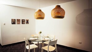 A dining area with a round glass table, white chairs, and two hanging wicker lamps. - Residenciales H1 & H2 (Santiago de los Caballeros)