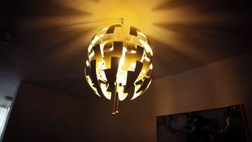 A spherical chandelier with a geometric pattern, hanging from a ceiling in a room with a plain wall and a painting.