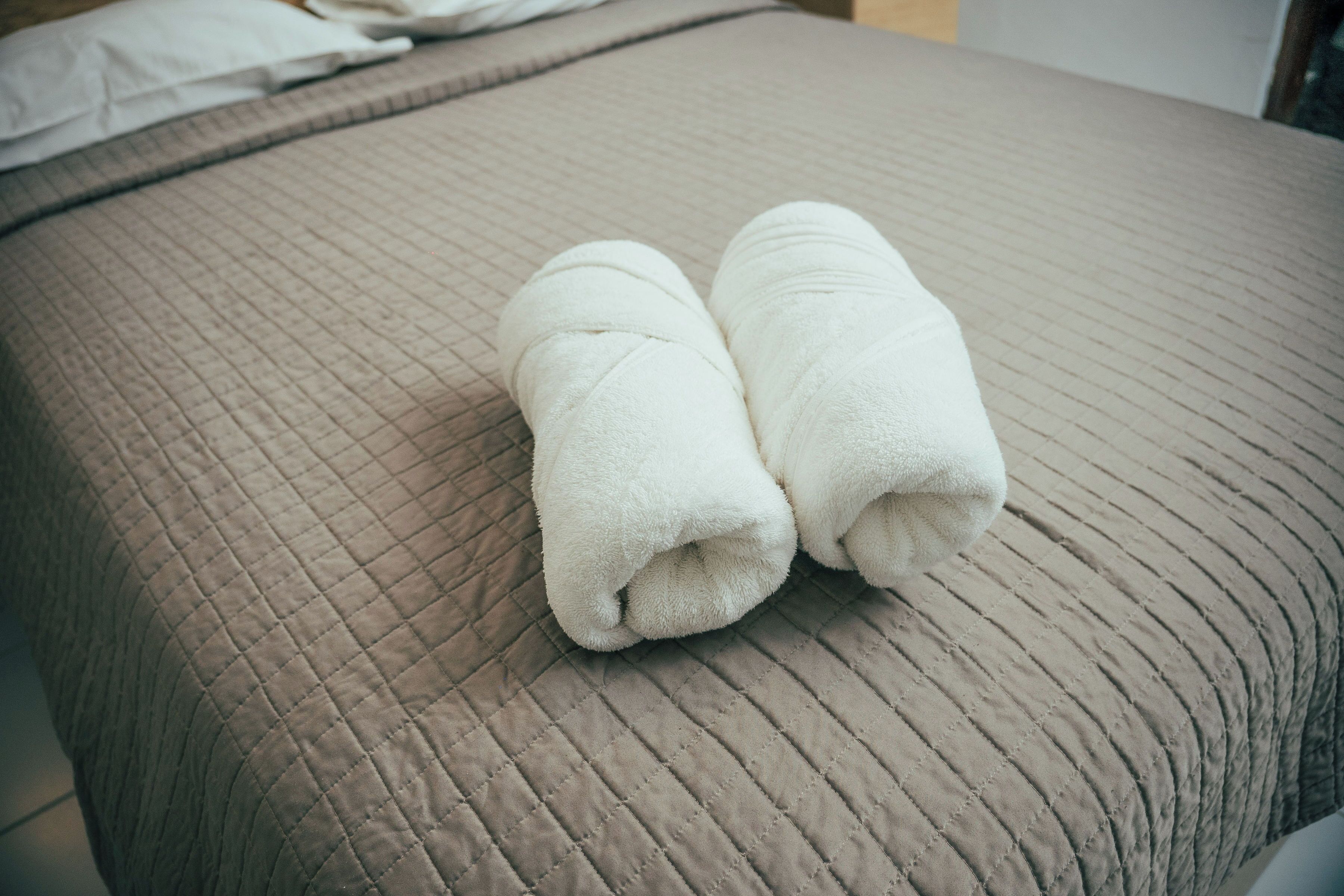 Una cama con cabecera acolchada y dos toallas enrolladas encima.