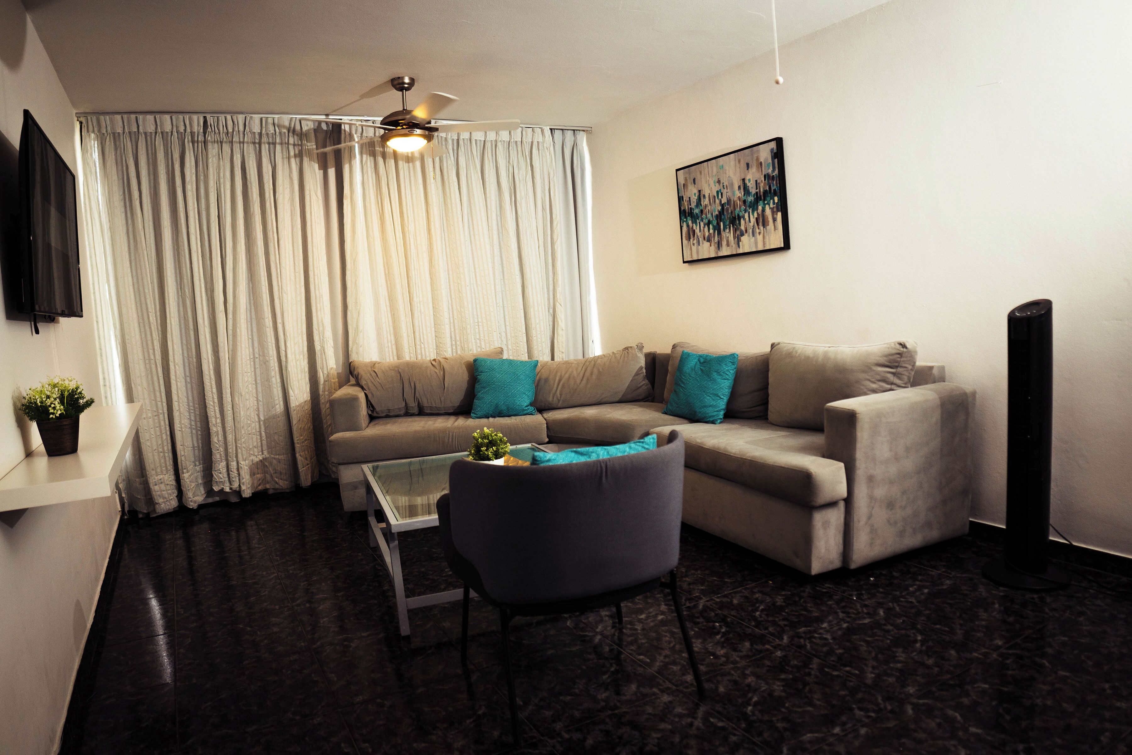 Ein Wohnzimmer mit Sofa, Sessel, Couchtisch, Deckenventilator, Fernseher und einem Bild an der Wand.