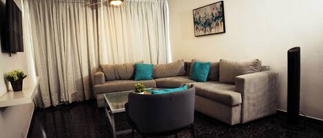 Ein Wohnzimmer mit Sofa, Sessel, Couchtisch, Deckenventilator, Fernseher und einem Bild an der Wand.