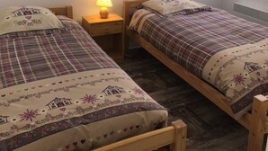 Ein Schlafzimmer mit zwei hölzernen Betten, einem Nachttisch mit Lampe, einem gerahmten Bild an der Wand und einem Fenster mit herzerwärmenden Vorhängen.
