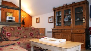 Ein gemütliches Wohnzimmer mit einem Holzkabinett, einer Couch mit gemusterten Kissen und einem Tisch mit einer weißen Schachtel.