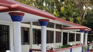 A covered outdoor area with white columns and blue accents, surrounded by potted plants and a white fence. - Sunapur Mini Resort (Bhurbhuria)