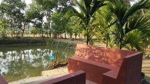 A serene outdoor area with a pond, surrounded by lush greenery and a red bench. - Sunapur Mini Resort (Bhurbhuria)