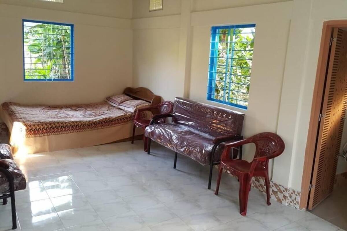 A room with a bed, two chairs, a small table, and a window with blue bars.