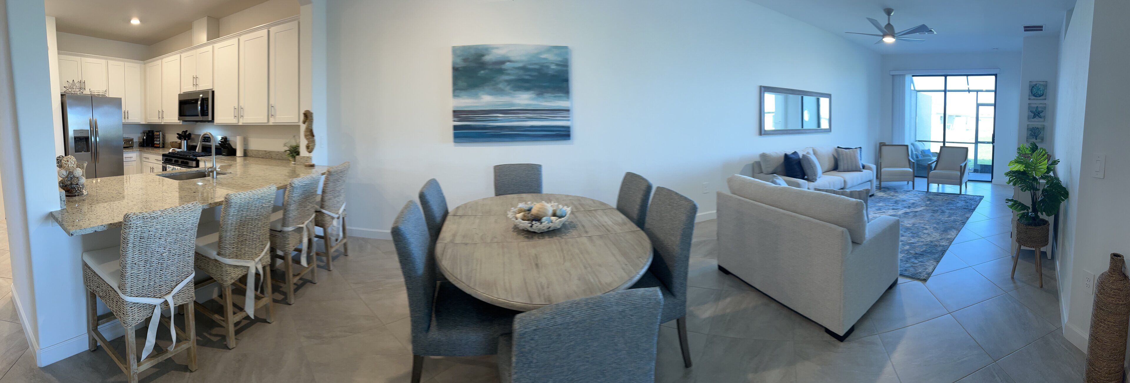 A modern kitchen with white cabinets, a stainless steel refrigerator, and a dining area with a round table and chairs.