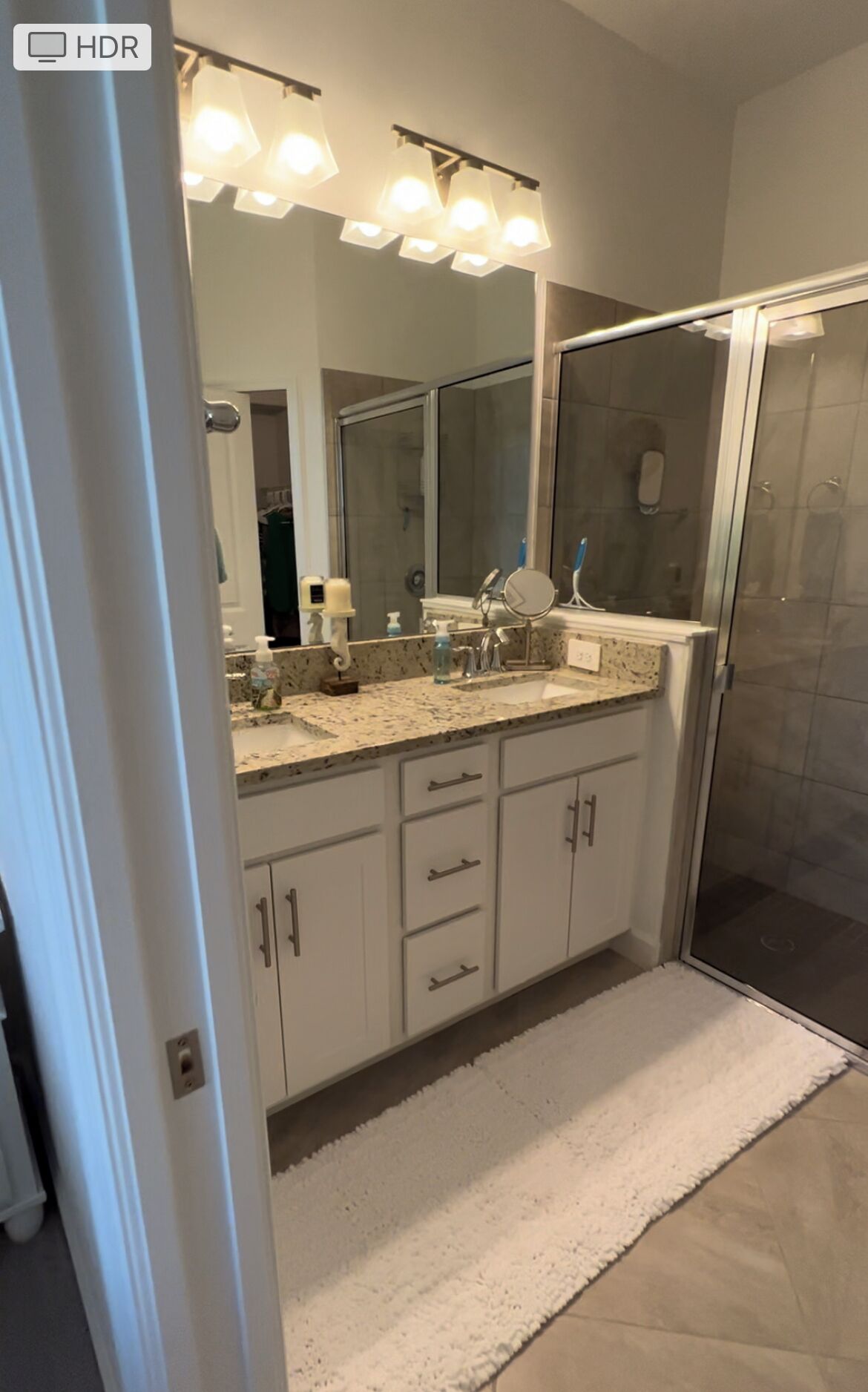 A modern bathroom with a large mirror, a shower enclosure, and a vanity with a sink and countertop.