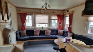 A compact RV interior with a sectional sofa, a dining area, and a kitchenette.