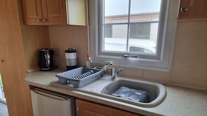 A compact kitchen with a sink, a dish rack, a kettle, and a bottle of dish soap.