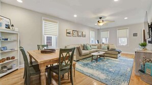 A spacious living room with a wooden dining table, a sofa, and a ceiling fan. - Beach Block Family House w/Garage & Decks (Sea Bright)