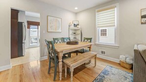 A dining area with a wooden table and chairs, a bench, a window with blinds, and a refrigerator in the background. - Beach Block Family House w/Garage & Decks (Sea Bright)