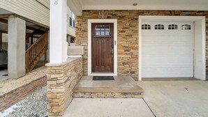 A residential house with a stone facade, a wooden front door, and a white garage door. - Beach Block Family House w/Garage & Decks (Sea Bright)