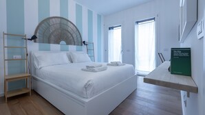 A modern bedroom with a large bed, a standing fan, a wooden shelf, and a book on the wall. - Italianway Comfort - Piranesi 18 B City Garden (Milan)