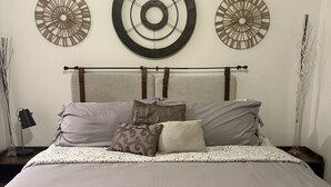 A neatly made bed with a headboard, two wall-mounted air conditioners, and three decorative wall clocks. - Midtown’s Hidden Secret (Reno)