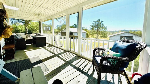 A covered porch with a wooden floor, wicker furniture, and a view of a rural landscape.