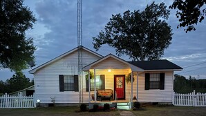 A single-story white house with a porch, a red door, and a white picket fence.