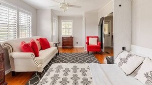 A bedroom with a bed, a white sofa with red cushions, a red armchair, and a ceiling fan.