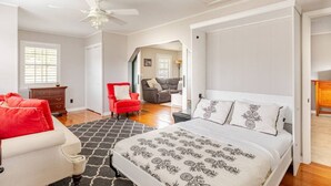 A bedroom with a bed, a red chair, a white sofa, and a wooden dresser.