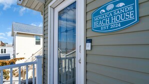 Talo, jonka edessä on kyltti, jossa lukee: ”Mosaica Sands Beach House, perustettu vuonna 2024”.
