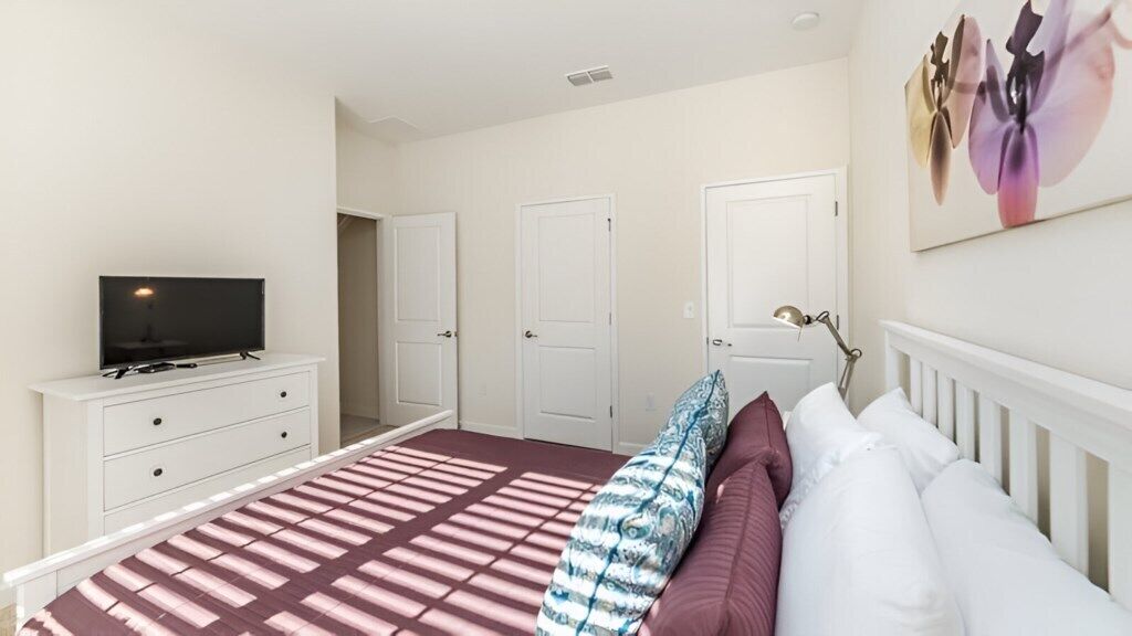A bedroom with a bed, a TV on a dresser, and a door leading to another room.