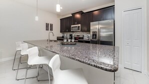 A modern kitchen with dark cabinets, stainless steel appliances, a granite countertop, and white bar stools.