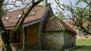 Un edificio rústico de piedra con techo inclinado, un pequeño porche y un patio cubierto de césped.