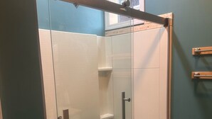 A glass-enclosed shower with a wooden beam above, white tiled walls, and a window with a view. - Luxury Downtown Condo (Clearfield)