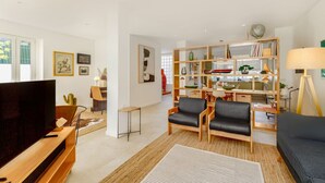 A modern living room with a flat-screen TV, two leather armchairs, a sofa, a bookshelf, and a dining area with a cactus and a lamp. - Haus Abel - with pool and garden in central Lisbon (Lisboa)