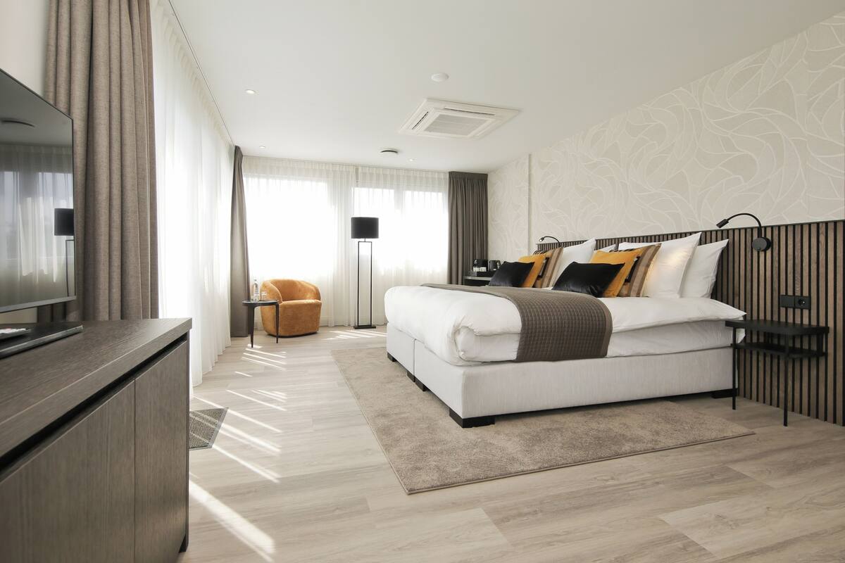 A modern hotel room with a large bed, a TV, a desk, and a chair.
