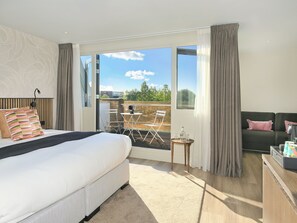 A hotel room with a bed, a small table with a bottle, a sofa, and a balcony with a table and chairs. - Boutique Hotel Hans (Badhoevedorp)