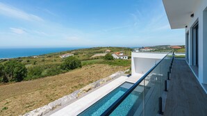 A modern building with a glass balcony overlooking a pool and a coastal landscape. - Axess Villa with panoramic ocean view (Lisboa)