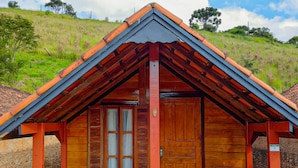 A wooden cabin with a pitched roof, a porch with seating, and a dog sitting outside. - Pousada Olivier da Montanha (Santo Antonio do Pinhal)