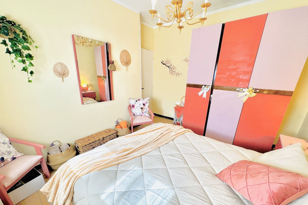 Um quarto com cama, uma cadeira, cômoda e espelho.
