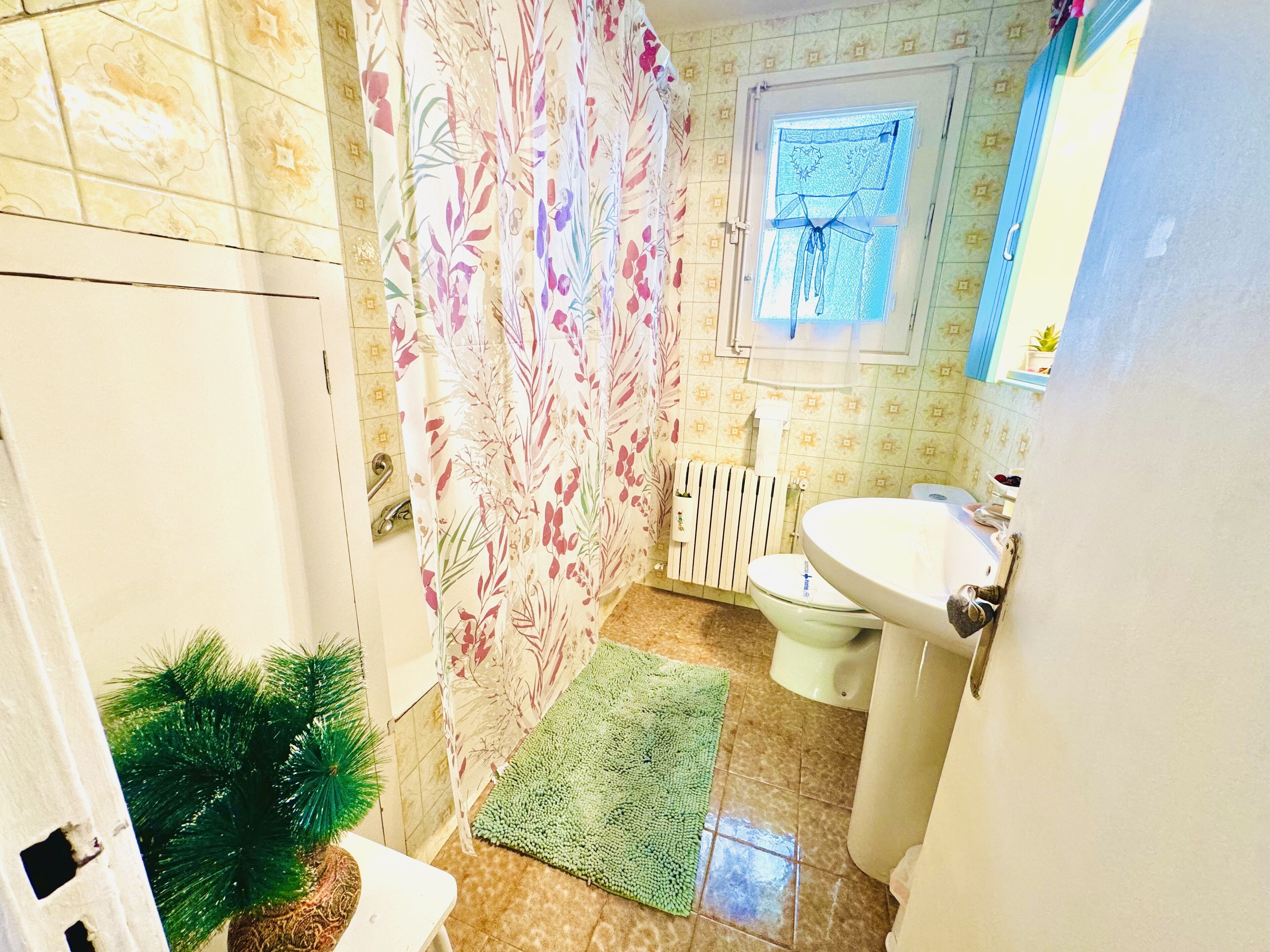 A small bathroom with a toilet, sink, shower curtain, and a small window.
