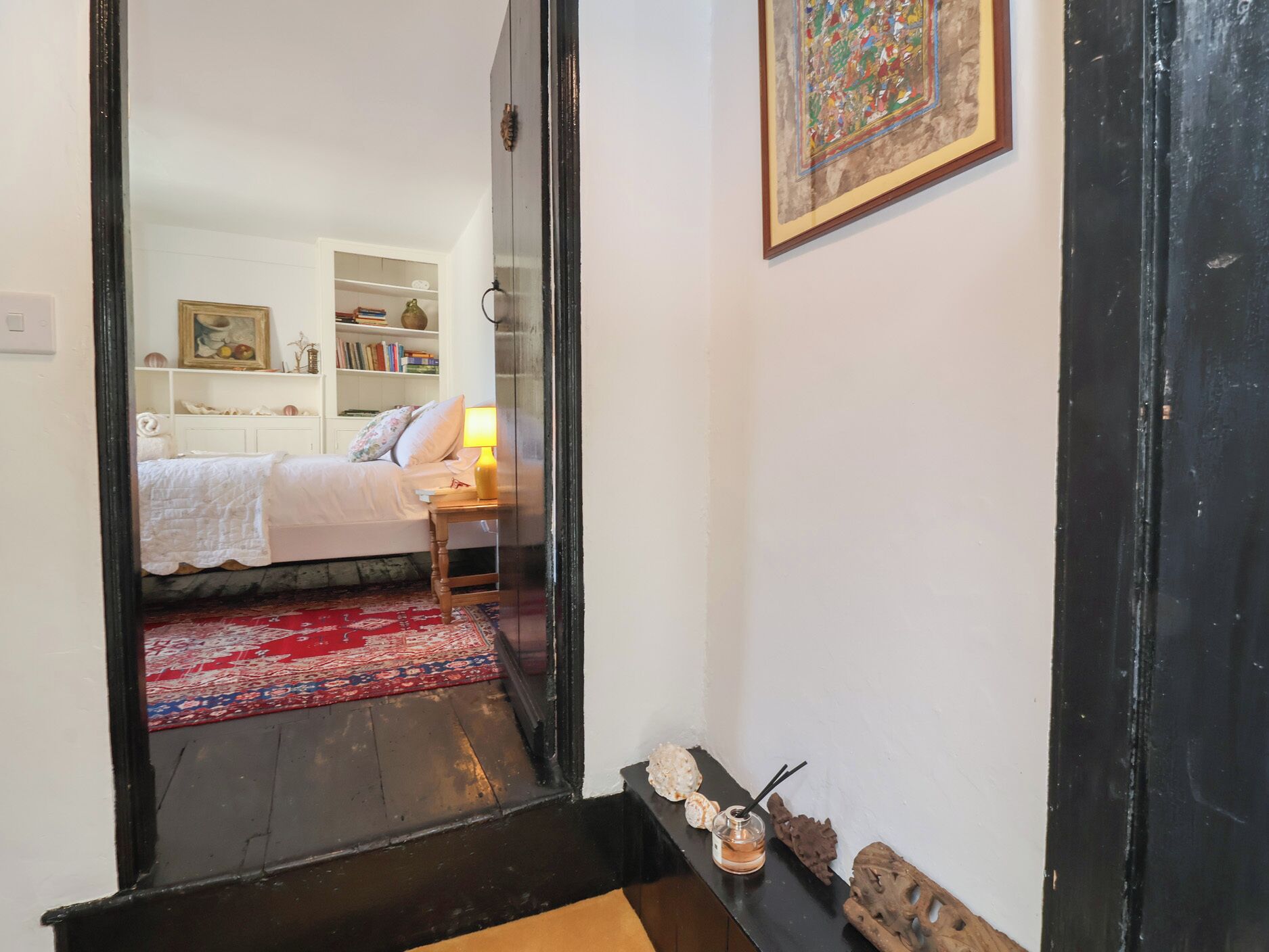 A bedroom with a bed, bedside table, lamp, and a red patterned rug.