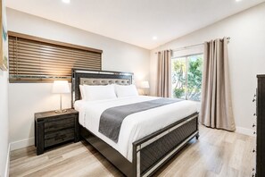 Un dormitorio moderno con una cama, mesitas de noche, una ventana con cortinas y vistas al verdor exterior.