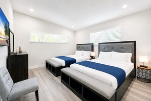 A hotel room with two beds, a desk, a chair, and a window with blinds.