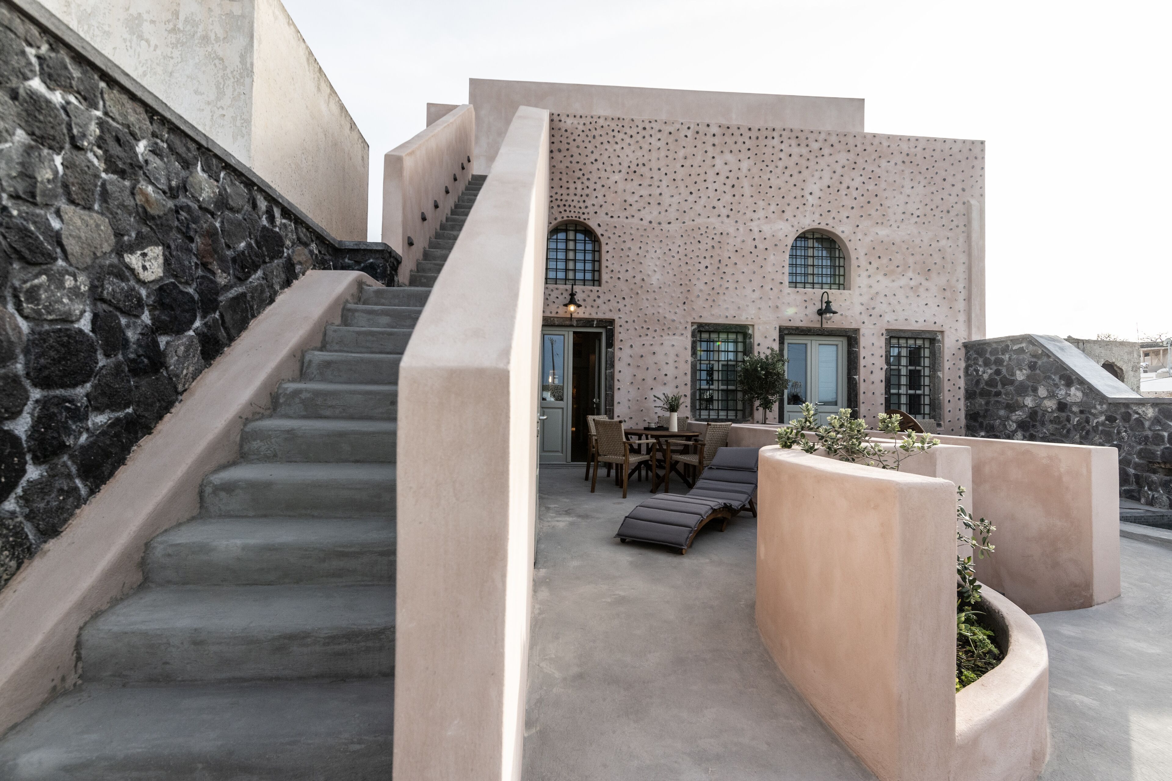 Un edificio moderno con una escalera de piedra, zona de estar al aire libre y una jardinera de concreto con plantas.