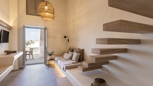 A modern interior with a sofa, a dining area, and a staircase with wooden steps. - Frescoes Luxury Suites (Santorini)