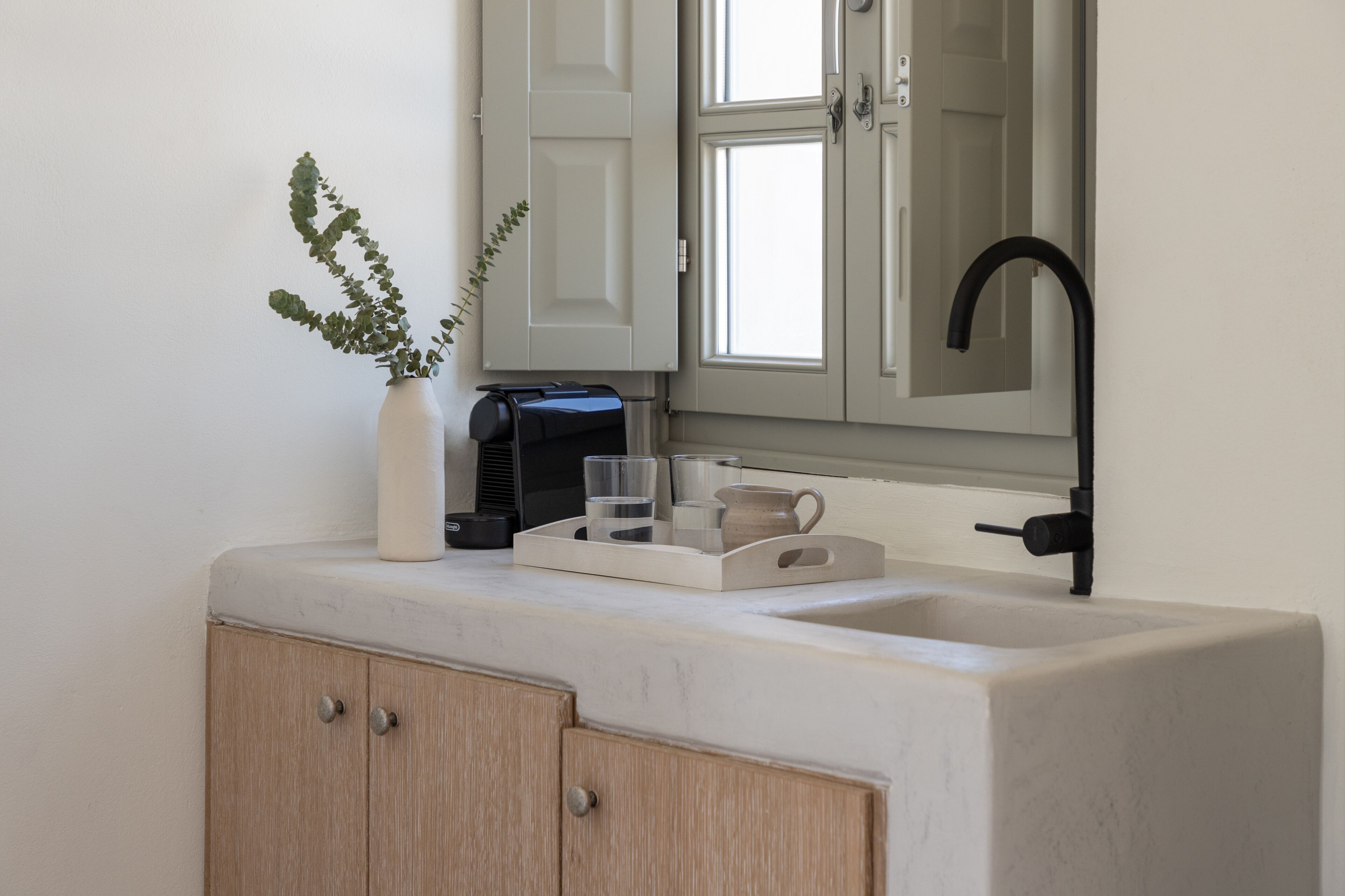 Un bagno moderno con lavandino bianco, mobili in legno, rubinetto nero, uno specchio e una pianta.