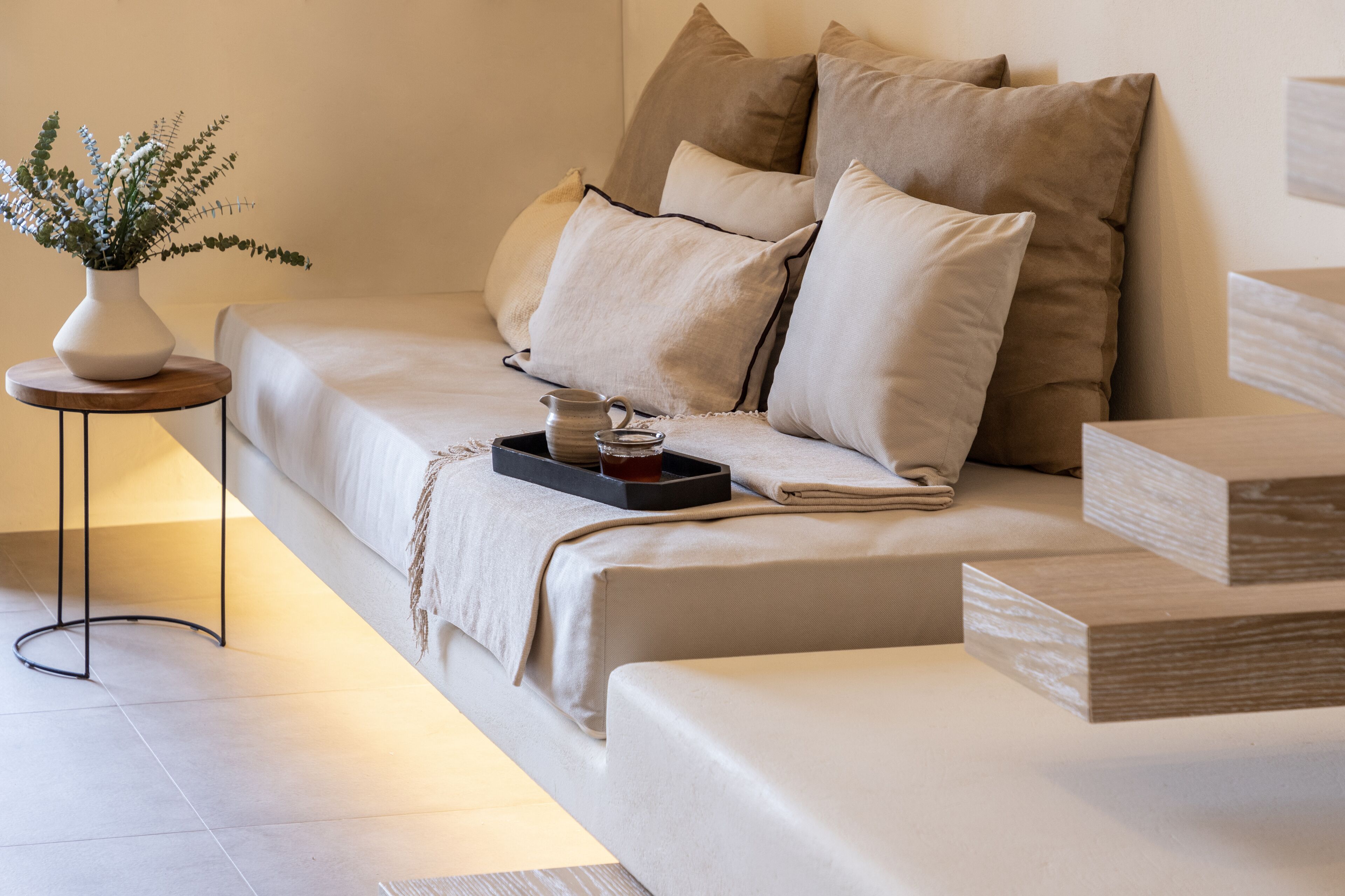 A modern bedroom with a sofa bed, a small side table, a vase with plants, and a tray with a cup and a book.