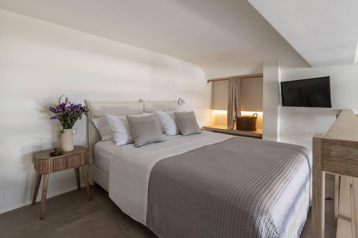 Un dormitorio moderno con una cama grande, mesitas de noche, un televisor de pantalla plana y un florero con flores.