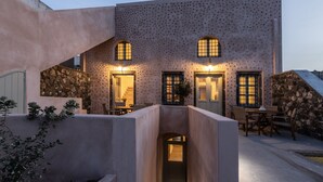 A modern building with a unique textured facade, arched windows, and a central entrance. - Frescoes Luxury Suites (Santorini)
