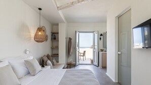 A bedroom with a bed, bedside table, and a hanging light fixture. There is a door leading to a balcony with a view of the sea. - Frescoes Luxury Suites (Santorini)