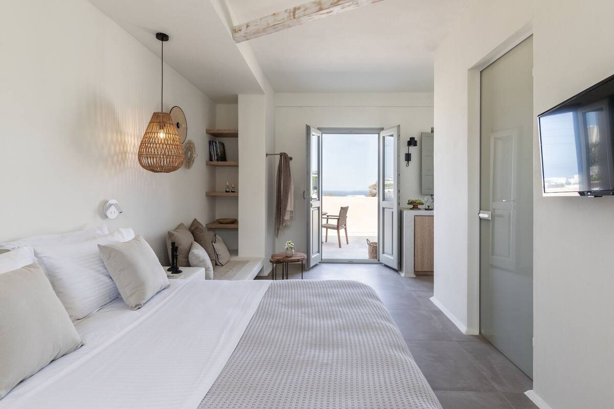 Un dormitorio con cama, mesita de noche y lámpara colgante. Hay una puerta que da a un balcón con vistas al mar.