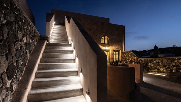 A staircase leading to a building with stone walls and a pool area. - Frescoes Luxury Suites (Santorini)