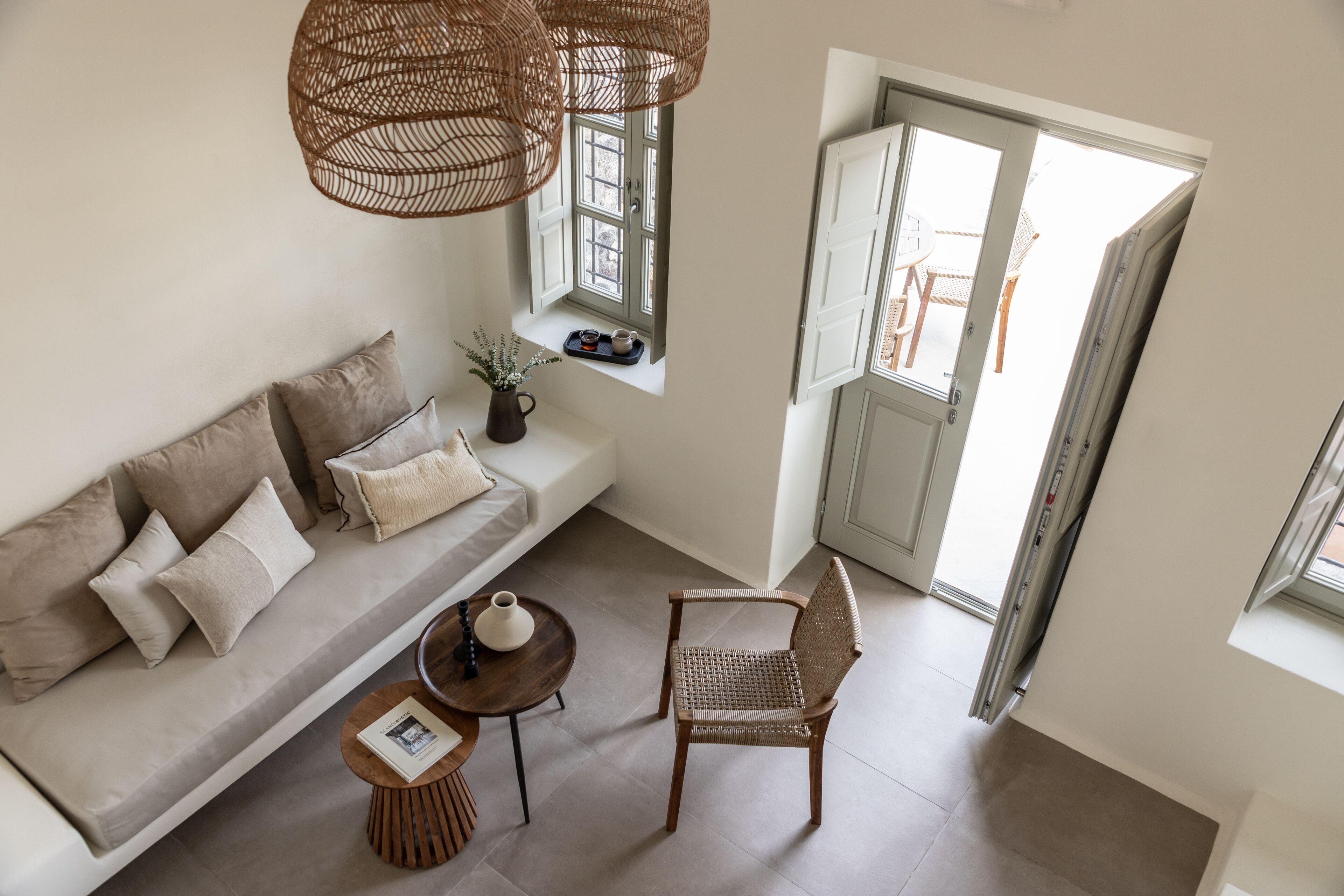 Ein modernes Wohnzimmer mit einer Couch, einem Korbsessel, einem kleinen Tisch und einem Fenster mit Blick ins Freie.