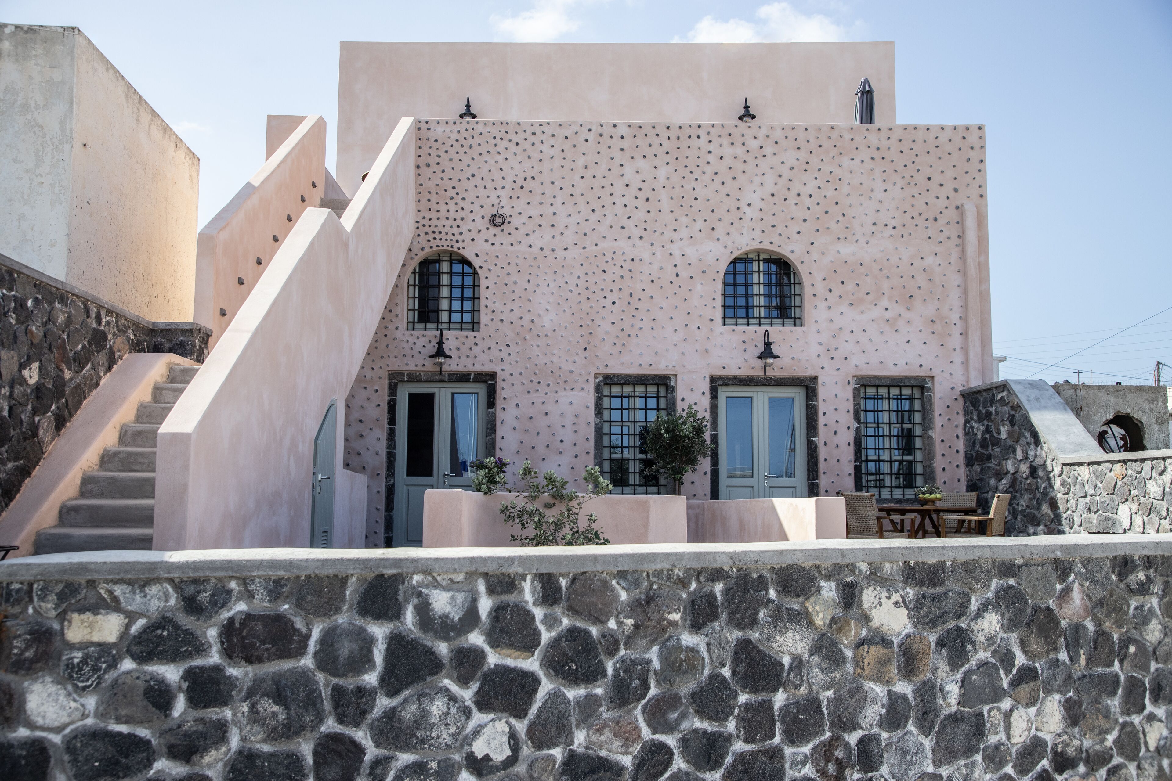 A building with a unique textured facade, a stone wall in the foreground, and a staircase leading up.