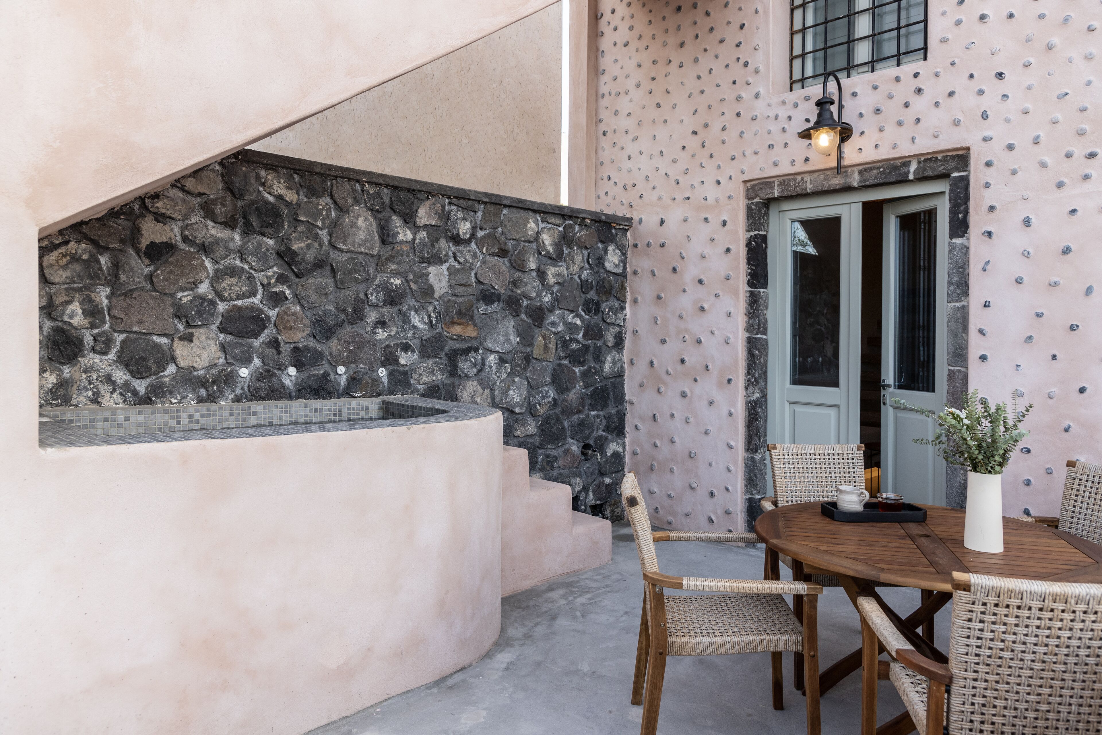 A stone wall, a wooden table with chairs, and a door with a light fixture.